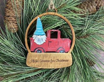 May include: Wooden Christmas ornament shaped like a snow globe with a gnome driving a red truck. The ornament has the text "I'll be Gnome for Christmas" on the bottom.