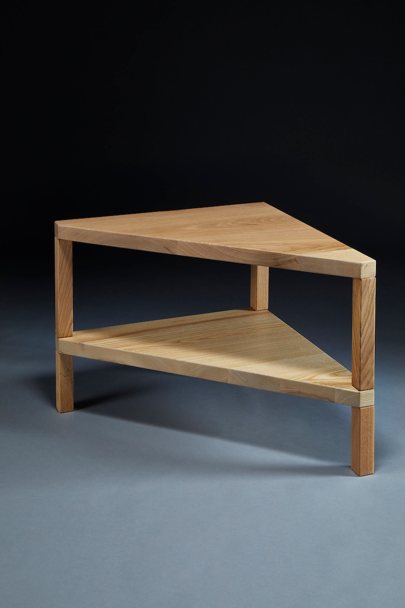 Pu&ograve; includere: Un tavolino da caff&egrave; triangolare in legno con un ripiano inferiore. Il tavolo &egrave; in legno chiaro e ha una finitura naturale.