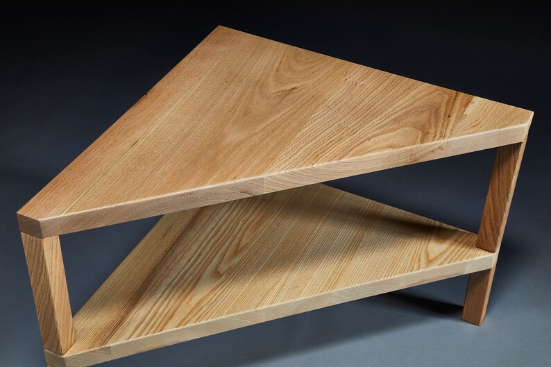 Pu&ograve; includere: Un tavolino da caff&egrave; triangolare in legno con un ripiano inferiore. Il tavolo &egrave; in legno chiaro con una finitura naturale.