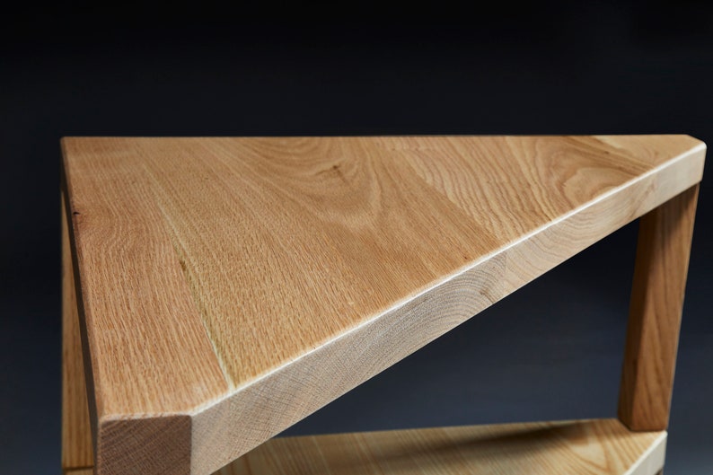 Pu&ograve; includere: Un tavolo in legno triangolare con una finitura marrone chiaro. Il tavolo ha un solo ripiano e tre gambe.