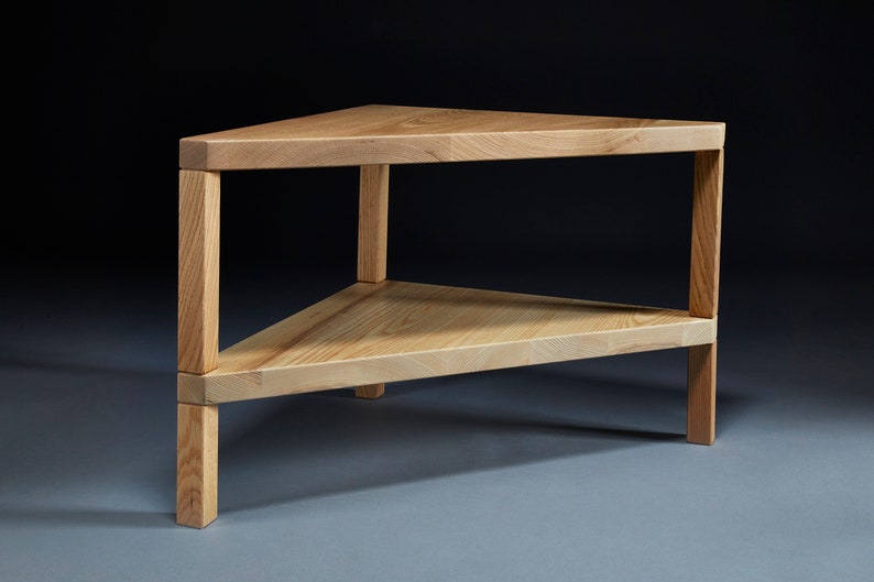 Pu&ograve; includere: Un tavolino da caff&egrave; triangolare in legno con due ripiani. Il tavolo &egrave; in legno chiaro e ha una finitura naturale.