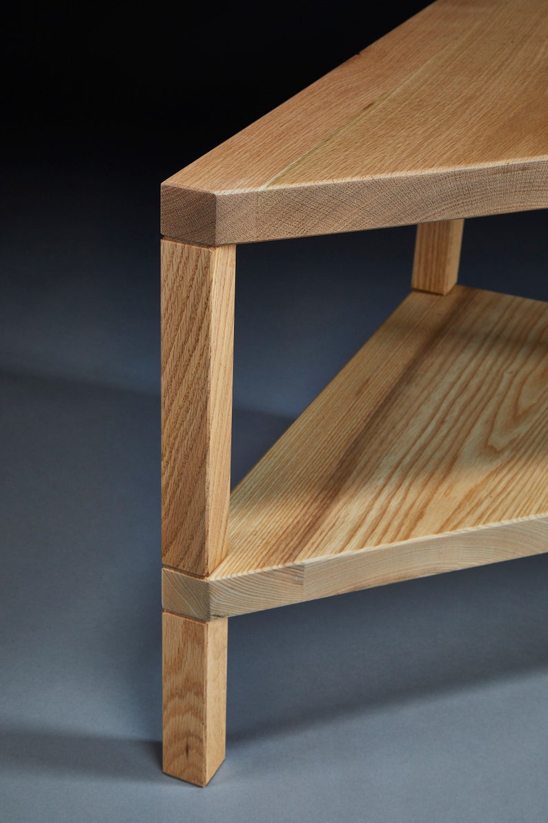 Pu&ograve; includere: Un tavolino da caff&egrave; triangolare in legno con un ripiano inferiore. Il tavolo &egrave; in legno chiaro con una finitura naturale. Il tavolo ha un design semplice e moderno.