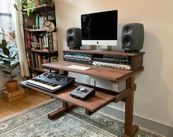 Könnte beinhalten: Ein hölzerner Musikproduktionstisch mit einer schwarzen Tastatur, einem Computermonitor und zwei grauen Lautsprechern. Der Tisch hat zwei Regale, eines für die Tastatur und eines für die Audio-Schnittstelle. Der Tisch ist aus dunklem Holz gefertigt und hat ein modernes Design.
