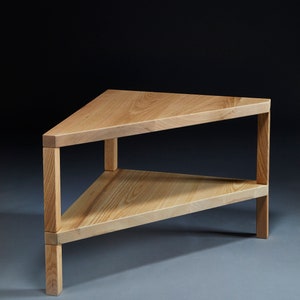 Pu&ograve; includere: Un tavolino da caff&egrave; triangolare in legno con due ripiani. Il tavolo &egrave; in legno chiaro e ha una finitura naturale.