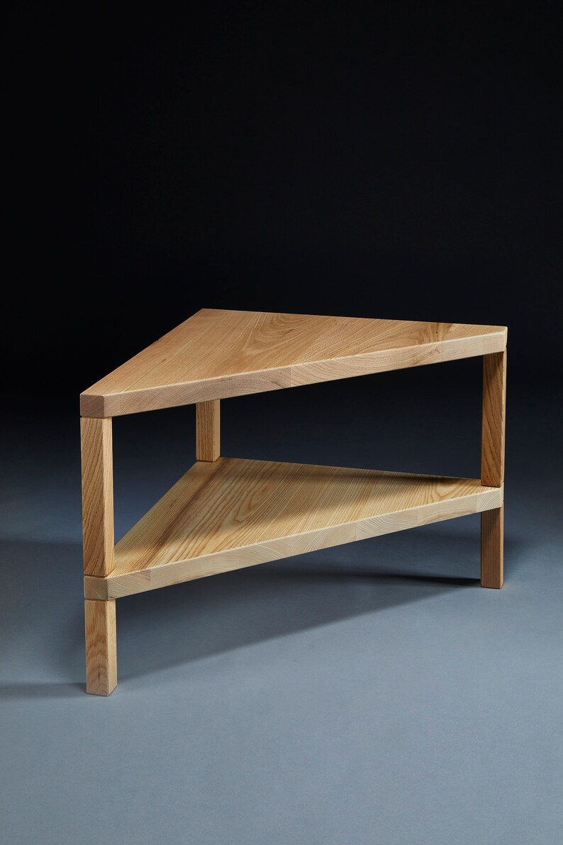 Pu&ograve; includere: Un tavolino da caff&egrave; triangolare in legno con due ripiani. Il tavolo &egrave; in legno chiaro e ha una finitura naturale.