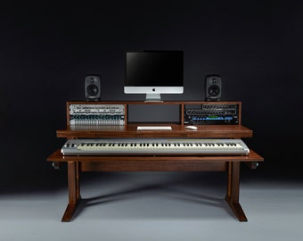 Puede incluir: Un escritorio de estudio de música de madera oscura con un teclado, un monitor de computadora y altavoces. El escritorio tiene un estante extraíble para el teclado.