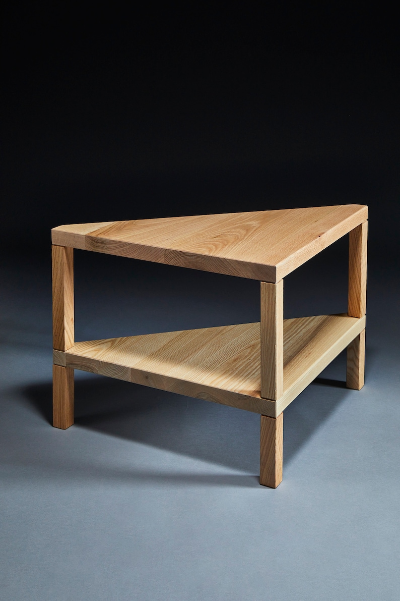 Pu&ograve; includere: Un tavolino triangolare in legno con due ripiani. Il tavolo &egrave; in legno chiaro e ha una finitura naturale.