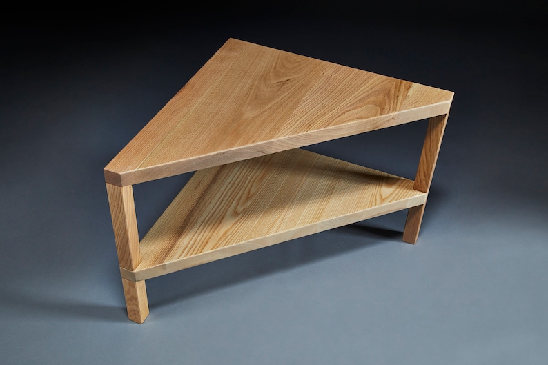 Pu&ograve; includere: Un tavolino da caff&egrave; triangolare in legno con due ripiani. Il tavolo &egrave; in legno chiaro e ha una finitura naturale.