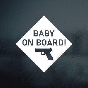 Può includere: Un cartello bianco a forma di diamante con la scritta "BABY ON BOARD!" e una sagoma nera di una pistola.