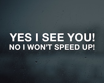 May include: A white sticker on a blurry background of raindrops on a window. The sticker reads "YES I SEE YOU! NO I WON'T SPEED UP!"