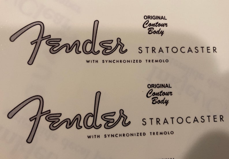 Może przedstawiać: Dwa czarno-białe naklejki na gitarę Fender Stratocaster z tekstem "ORIGINAL Contour Body" i "WITH SYNCHRONIZED TREMOLO".