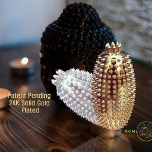 May include: Two spiked massage tools, one with a silver finish and one with a gold finish, are displayed on a wooden surface. The text "Patent Pending 24K Solid Gold Plated" is visible in the image.