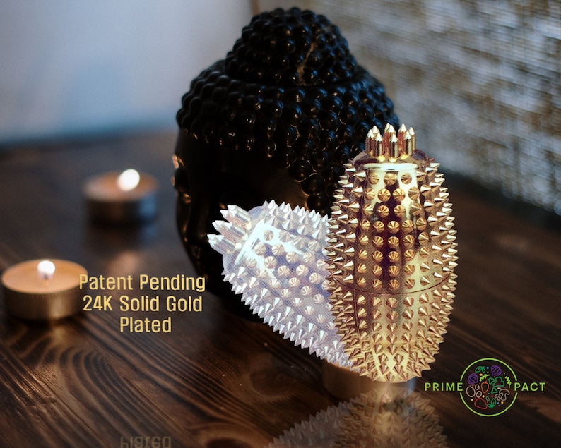 May include: Two spiked massage tools, one with a silver finish and one with a gold finish, are displayed on a wooden surface. The text "Patent Pending 24K Solid Gold Plated" is visible in the image.