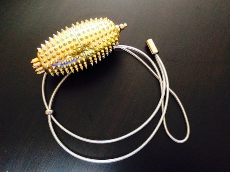 May include: A gold-coloured, spiky, oval-shaped pendant hangs from a silver chain. The pendant has a textured surface and appears to be made of metal.