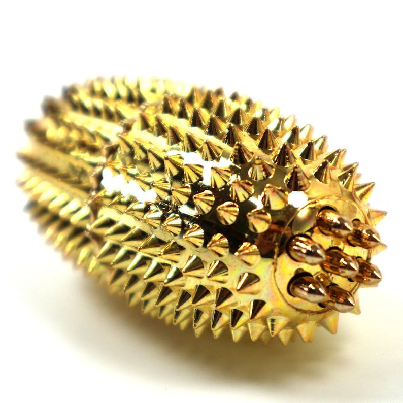 May include: A gold-coloured acupressure roller with a textured surface covered in small spikes. The roller has a handle with six smaller spikes on the end.