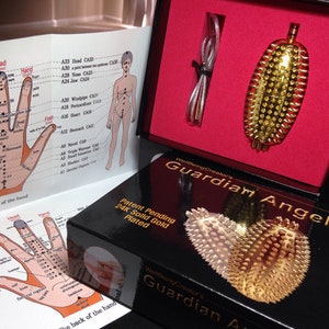 May include: A gold-plated Guardian Angel acupressure tool with a black box and a pamphlet with diagrams of the palm of the hand. The box has the text "Patent Pending 24K Solid Gold Plated" and "Guardian Angel".