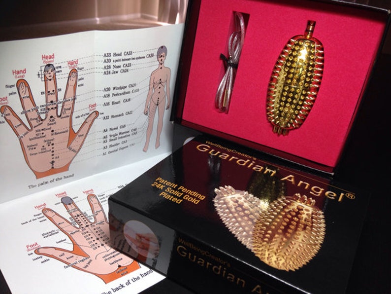 May include: A gold-plated Guardian Angel acupressure tool with a black box and a pamphlet with diagrams of the palm of the hand. The box has the text "Patent Pending 24K Solid Gold Plated" and "Guardian Angel".