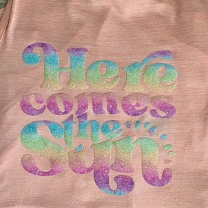May include: A pink t-shirt with a rainbow glitter design that says "Here comes the sun".