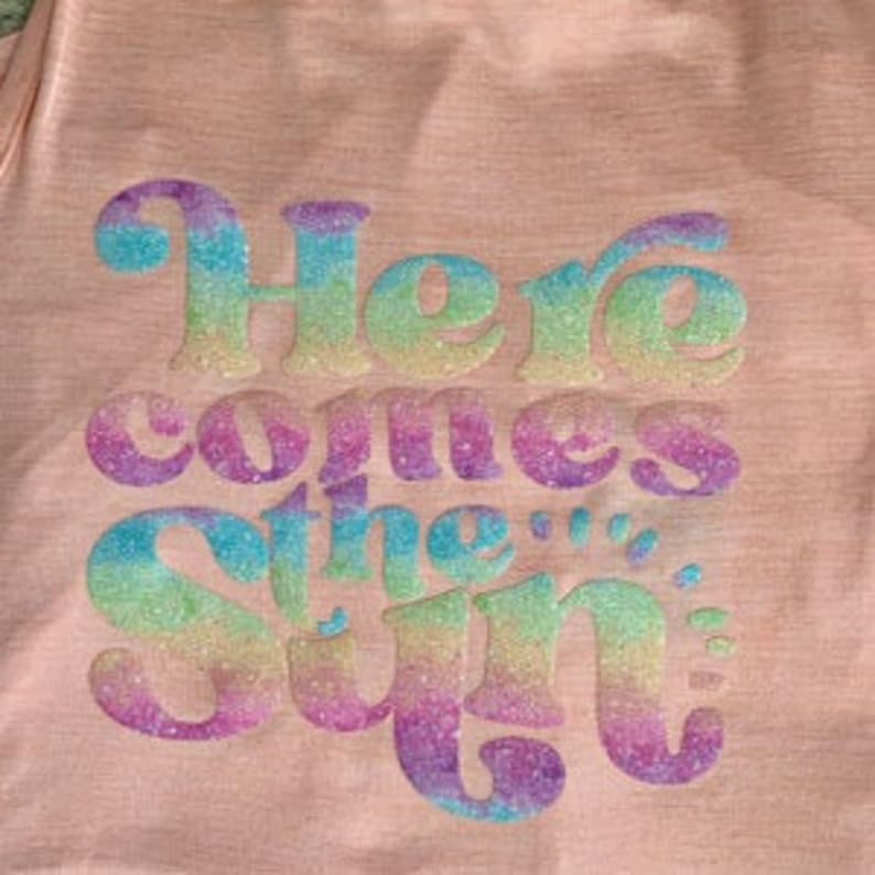 May include: A pink t-shirt with a rainbow glitter design that says "Here comes the sun".