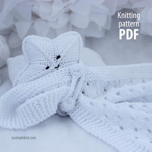 May include: A white knitted baby blanket and star-shaped hat. The hat has two black button eyes and a small smile. The blanket has a decorative edge and is made of soft, white yarn. Text in the image reads "Knitting pattern PDF" and "sosimpleknit.com".