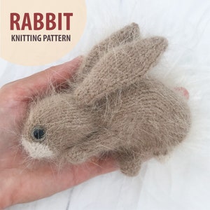 May include: A knitted brown rabbit toy with a white nose and black eyes. The toy is held in a hand.