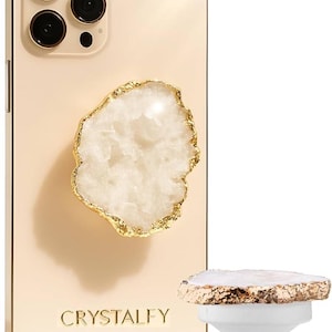 May include: A gold-colored phone case with a white and gold geode-style phone grip. The phone case has the word "CRYSTALFY" printed on it. A matching phone grip is detached and standing upright.