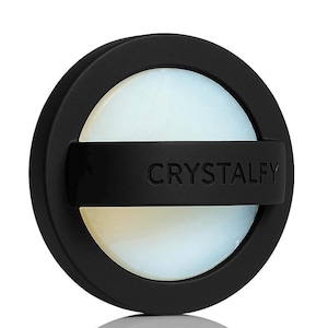 May include: A black round object with the word "CRYSTALFY" printed on a black band. The center of the object is a light, opalescent color.