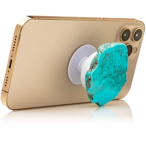 May include: A gold smartphone with a turquoise stone phone grip attached. The phone grip is white with the word "CRYSTALIFE" printed on it. The turquoise stone is a vibrant blue-green color.
