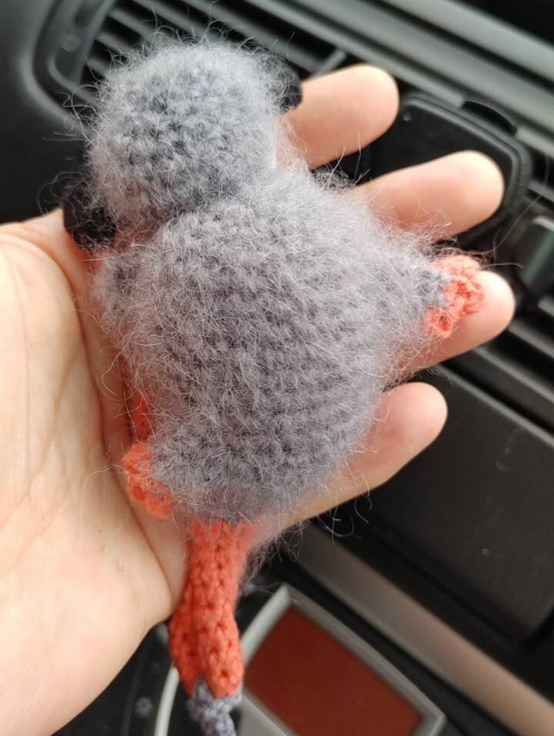 May include: A grey crocheted monkey toy with orange legs and tail. The toy is being held in a person's hand.