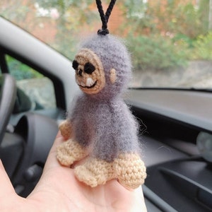 Puede incluir: Un mono de crochet gris con una cara de calavera y una cuerda negra que cuelga de su cabeza. El mono est&aacute; siendo sostenido en la mano de una persona.