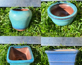 May include: Four bonsai pots in different shapes and sizes. The pots are all glazed in shades of blue and green, with a brown interior. The pots are sitting on a bed of green grass.