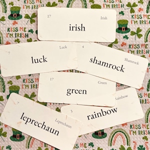 May include: A collection of St. Patrick's Day flashcards with words like "Irish," "luck," "shamrock," "green," "rainbow," and "leprechaun." The cards are arranged on a patterned background with shamrocks and the phrase "Kiss Me I'm Irish."