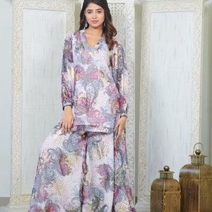 Può includere: Un set di top e pantaloni palazzo con stampa paisley bianca e viola. Il top ha un collo a V e maniche lunghe. I pantaloni sono larghi e fluidi.