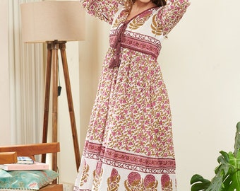May include: A white maxi dress with a pink and green floral print. The dress has a V-neckline, long sleeves, and a tie at the waist. The dress is made of cotton and has a flowy silhouette.