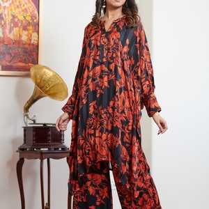 Pu&ograve; includere: Un completo pantalone nero e arancione con motivo, con una blusa a maniche lunghe e pantaloni a gamba larga. La blusa ha un collo a V e una chiusura con bottone. I pantaloni hanno una vestibilit&agrave; rilassata.