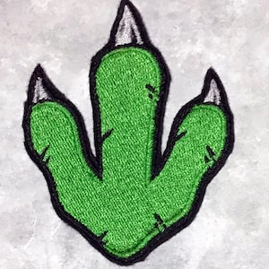 May include: Green dinosaur footprint patch with black outline and three white claws.