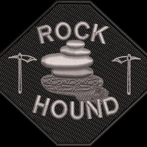 May include: A black and gray embroidered patch with the text "ROCK HOUND" in a white font. The patch features a stack of gray rocks and two gray pickaxes.