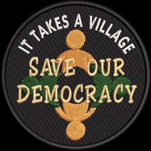 May include: Embroidered patch with the text "IT TAKES A VILLAGE" in white, arched around the top. Below, "SAVE OUR DEMOCRACY" in gold lettering. The design includes gold and green figures on a black background.