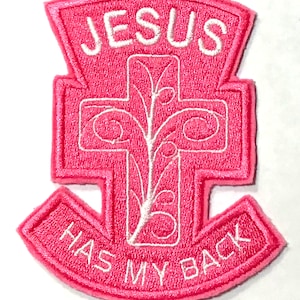 May include: Pink embroidered patch with a white cross and a vine design. The text "JESUS HAS MY BACK" is embroidered in white.