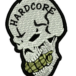 May include: Embroidered patch featuring a skull design with the word "HARDCORE" arched across the top. The skull is white with black accents and a green grenade in its mouth, all outlined in black.