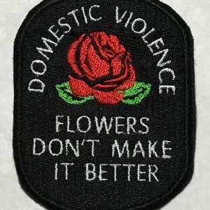 May include: Black embroidered patch with a white outline. The patch features a red rose with green leaves and the text "Domestic Violence Flowers Don't Make It Better".
