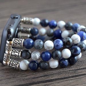 Puede incluir: Un Apple Watch negro con una banda de cuentas multi-hilo. La banda está hecha de piedras azules, blancas y grises.