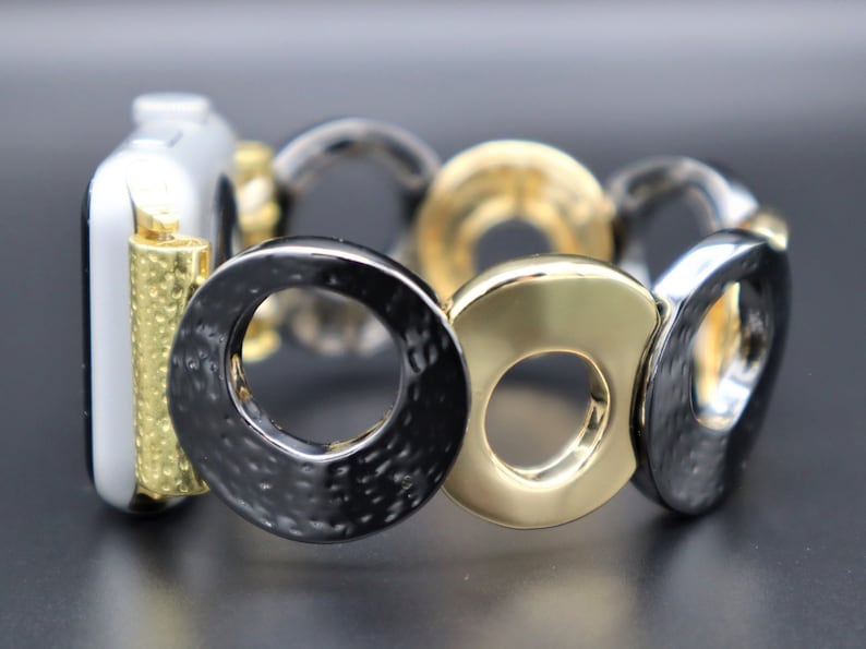 May include: A black and gold metal watch band with a textured finish. The band is made up of interlocking circles.