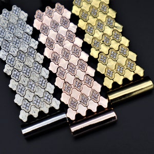 May include: Three metal watch bands with a geometric pattern and clear stones. The bands are silver, rose gold, and gold.