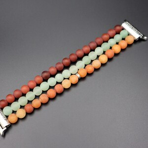 May include: A multi-colored beaded Apple Watch band with three rows of beads in shades of red, orange, and green. The band is made of smooth, round beads and has a silver metal clasp.