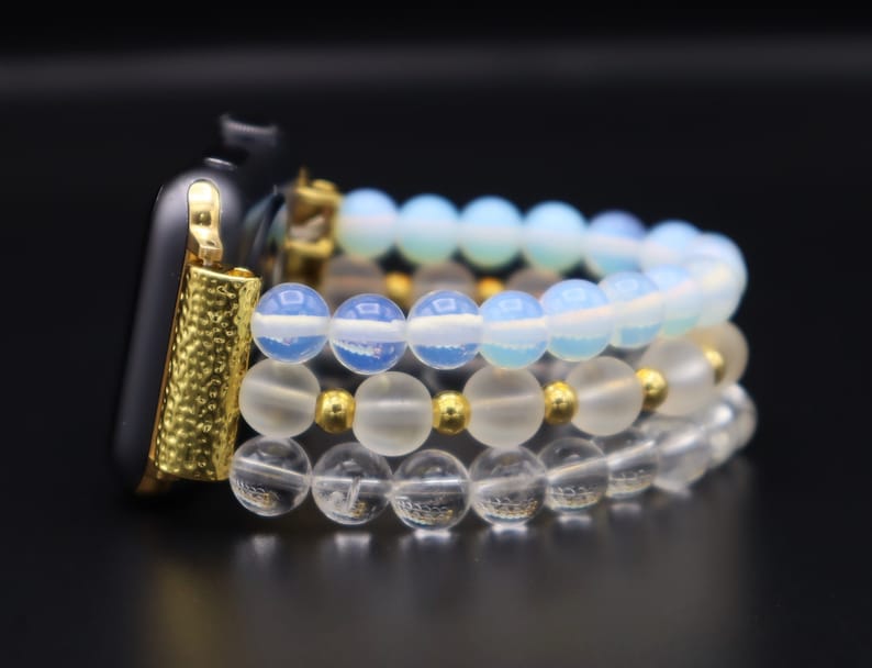 K&ouml;nnte beinhalten: Ein goldenes Armband mit drei Schichten Perlenarmb&auml;ndern. Die oberste Schicht ist hellblau, die mittlere Schicht ist wei&szlig; und die unterste Schicht ist klar.