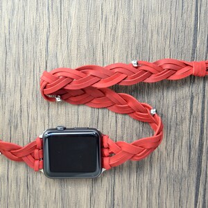 May include: A red braided leather watch band with a silver clasp and tassel. The band is designed to fit an Apple Watch.