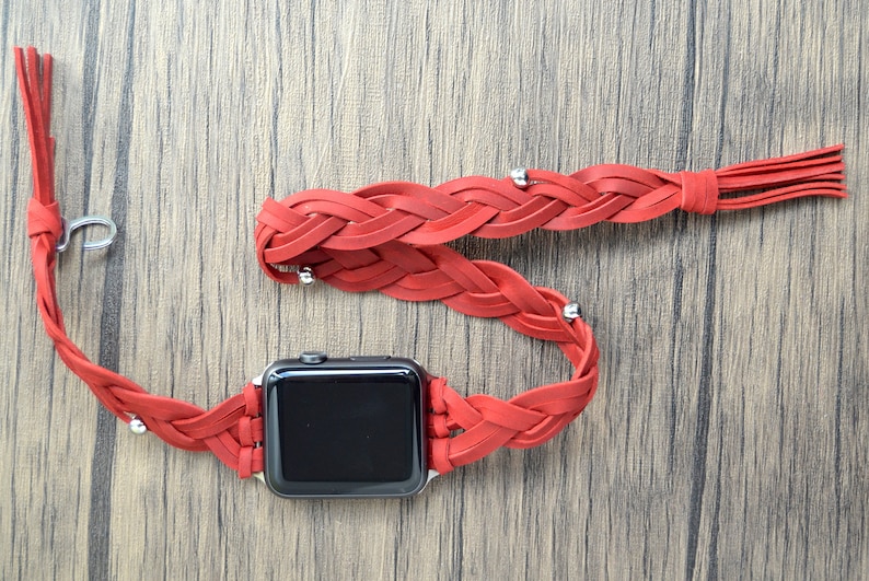 May include: A red braided leather watch band with a silver clasp and tassel. The band is designed to fit an Apple Watch.
