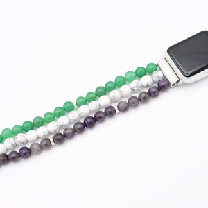 May include: A green, white, and purple beaded Apple Watch band. The band is made of three strands of beads, with the green beads on the top, the white beads in the middle, and the purple beads on the bottom.