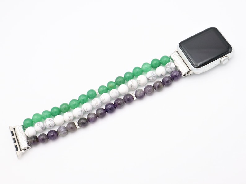 May include: A green, white, and purple beaded Apple Watch band. The band is made of three strands of beads, with the green beads on the top, the white beads in the middle, and the purple beads on the bottom.